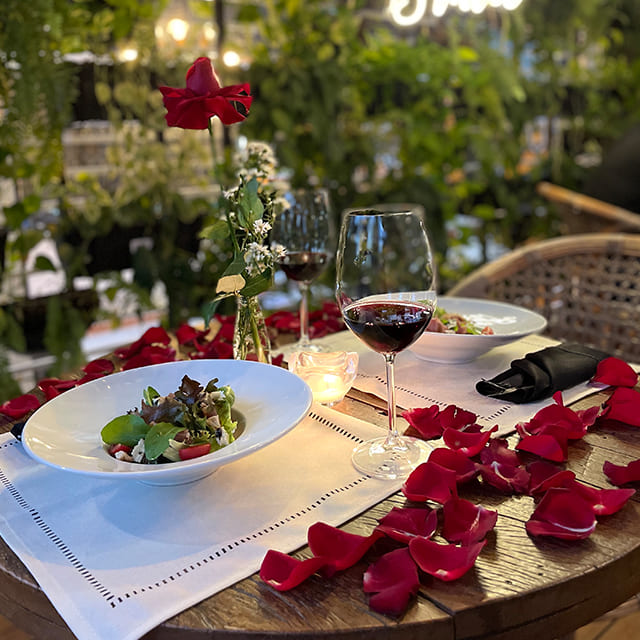 Mesa decorada com vela acesa e pétalas de rosas vermelhas
