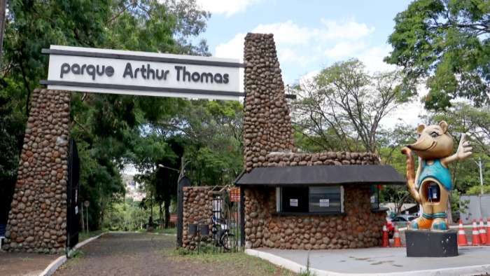 Entrada do parque Arthur Thomas, apresentando sua famosa estrutura de pedra e uma escultura de um personagem divertido, rodeado por árvores. Com o intuito de economizar com passeios gratuitos